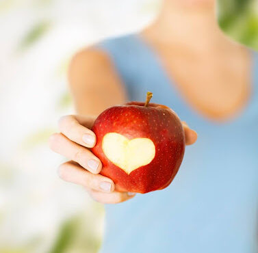 heart healthy lifestyle -woman holding out an apple with a heart-shaped bite in it